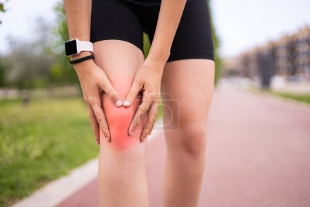 Téléchargez les photos : Athlète féminine tenant le genou dans la douleur lors de l'entraînement de course en plein air - en image libre de droit