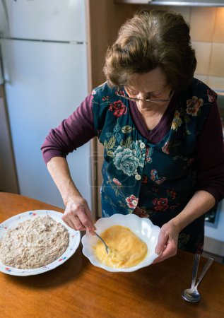 Vertikales Foto mit erhöhtem Blick auf eine alte Frau, die zu Hause Eier schlägt und handgemachte Kroketten herstellt
