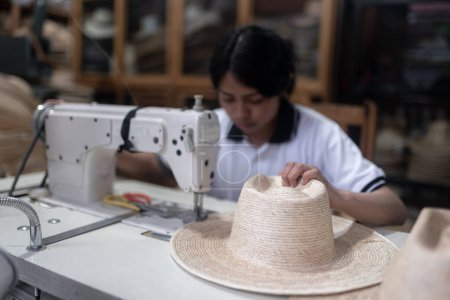 Eine junge hispanische Frau näht in einer traditionellen Werkstatt in Guatemala mit einer Maschine einen Naturfaserhut