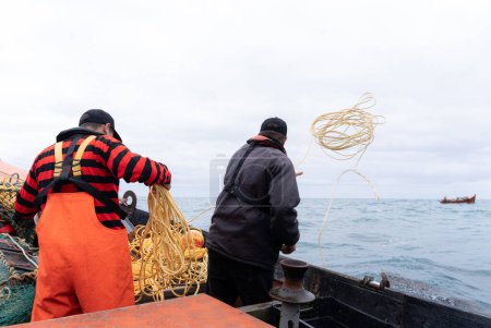 Foto de Dos pescadores tirando redes para atrapar langostas en el mar de pie en un barco - Imagen libre de derechos
