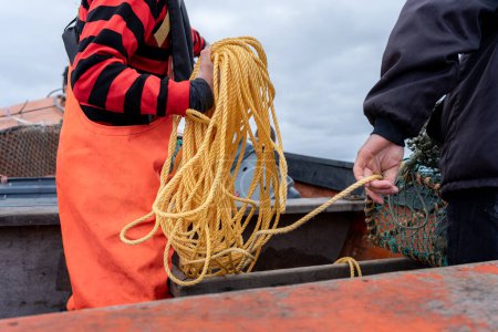 Fischer, der ein Seil hält, um das Fischernetz zu holen, während Hummer ein Boot bilden