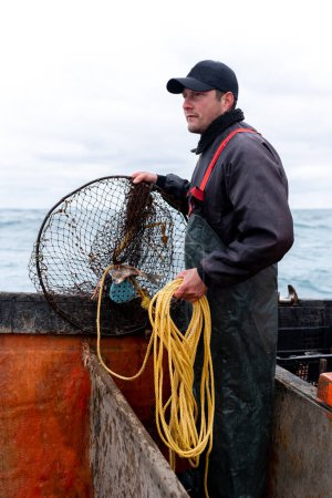 Vertikales Foto eines erwachsenen kaukasischen Fischers bei der Arbeit, der ein Netz aus dem Wasser zieht