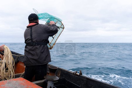 Fisherman using container with net to fish lobsters standing on a boat in the sea