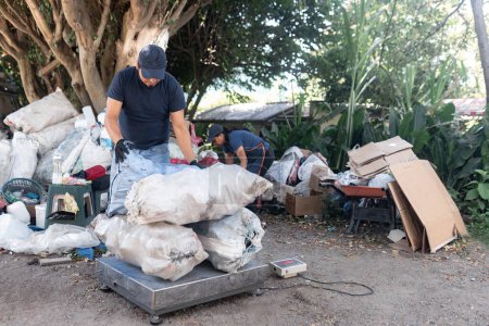 Photo for A Hispanic man weighs a pile of sacks of reclaimed materials, supported by a woman in the background - Royalty Free Image