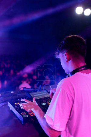 Vista trasera vertical de un DJ mezclando en el escenario usando tablero