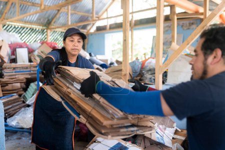 Collaborative teamwork in recycling as a young Hispanic woman receives a stack of recycled cardboard from her partner at a recycling facility.