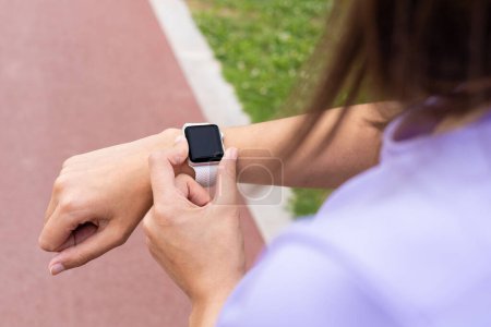 Foto de Mujer con un reloj de seguimiento de fitness para monitorear el entrenamiento en un parque urbano. Bienestar, salud y estilo de vida activo. - Imagen libre de derechos