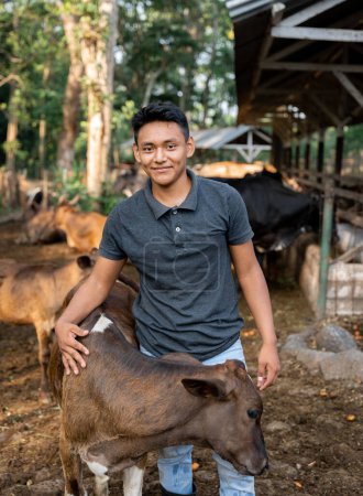 Photo for Hispanic Young Man Huging a Calf in in Dairy Farm, capturing the interaction between caretaker and young animal - Royalty Free Image