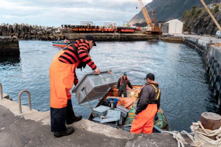 Équipe de plusieurs pêcheurs déchargeant des caisses de homards fraîchement pêchés au port par une journée nuageuse et froide