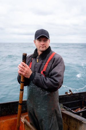 Vertical portrait of a young fisherman wearing work uniform clothes on a boat