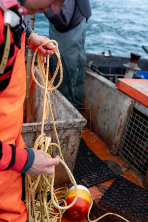 Vertical close-up of a young male fisherman working with a rope on a lobster fishing boat