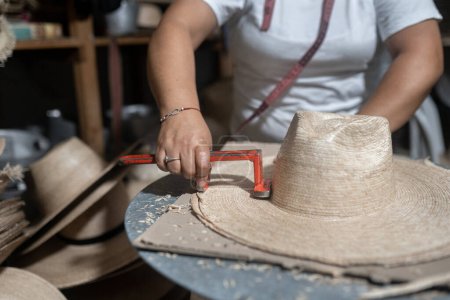 Schneiden der Krempe eines traditionellen Naturfaserhuts während des Produktionsprozesses in einer traditionellen Werkstatt in Guatemala