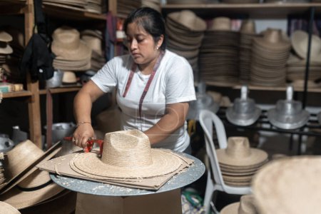 Eine erwachsene hispanische Frau schneidet in einer traditionellen Werkstatt in Guatemala den Rand eines Naturfaserhuts