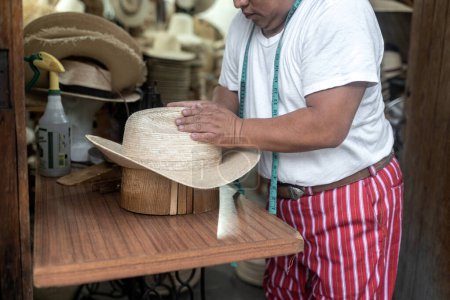 Photo for An adult Hispanic man is shaping a natural fiber hat using a wooden block in a traditional workshop in Guatemala - Royalty Free Image
