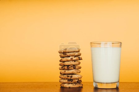 Photo for Inviting breakfast scene: cookies and milk on a rustic table with an orange backdrop. Perfect for marketing. - Royalty Free Image