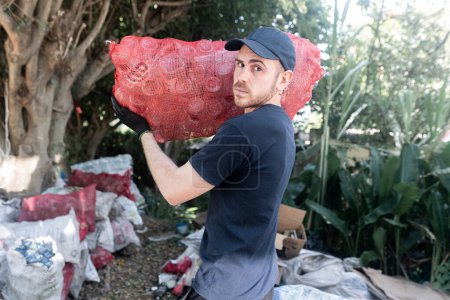 A serious young man holds a bag filled with recycled crystal bottles at a recycling facility. His determined look shows his dedication to the environment and hard work in recycling