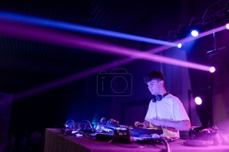 Téléchargez les photos : Horizontal photo with wide view and copy space of a concentrated DJ performing on a night club with neon lights - en image libre de droit
