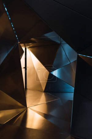 Téléchargez les photos : Mur 3D moderne avec motif géométrique créatif placé près de la lumière chatoyante dans un studio spacieux avec un style futuriste et un éclairage tamisé - en image libre de droit