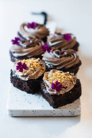 Foto de Alto ángulo de tortas de esponja de chocolate vegano con crema batida y decoraciones de flores servidas en la tabla de cortar en la panadería - Imagen libre de derechos