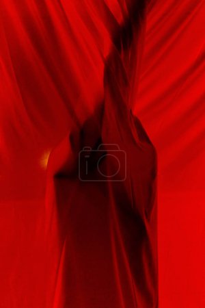 Foto de Persona misteriosa irreconocible escondida detrás de cortinas de luz translúcidas rojas mientras está de pie en el balcón oscuro en el apartamento en la noche oscura - Imagen libre de derechos