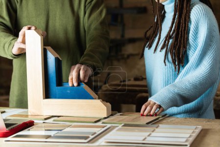 Photo for Crop carpenter standing at workbench with wooden detail and tools with laptop while discussing order with customer - Royalty Free Image