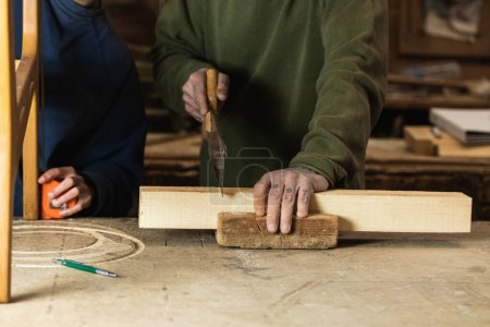 Photo for Unrecognizable carpenters cutting with saw and measuring woodwork with tape while creating wooden details in workshop - Royalty Free Image