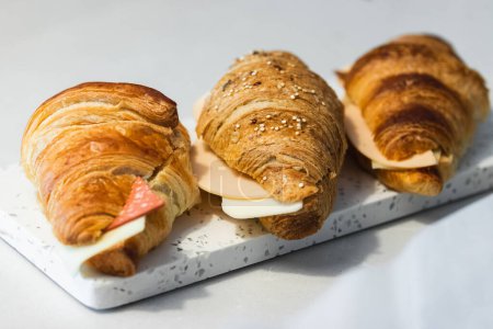 Photo for Delicious fresh croissants with slices of cheese and ham served on tray on table - Royalty Free Image