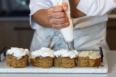 Téléchargez les photos : Cultiver anonyme cuisinier avec sac à pâtisserie avec crème décoration végétalien gâteaux aux carottes tout en préparant des desserts dans la boulangerie - en image libre de droit