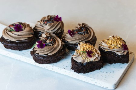 Téléchargez les photos : Gâteaux d'éponge au chocolat végétalien avec crème fouettée et décorations florales servis sur planche à découper sur table dans une boulangerie - en image libre de droit