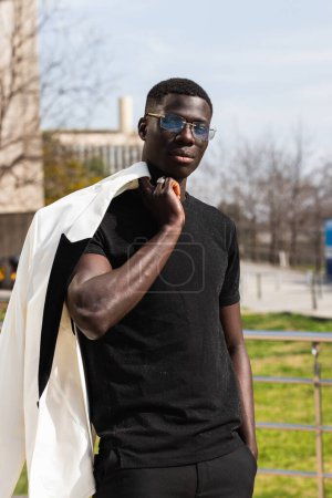 Téléchargez les photos : Jeune entrepreneur noir confiant avec veste et main dans la poche regardant la caméra en ville - en image libre de droit