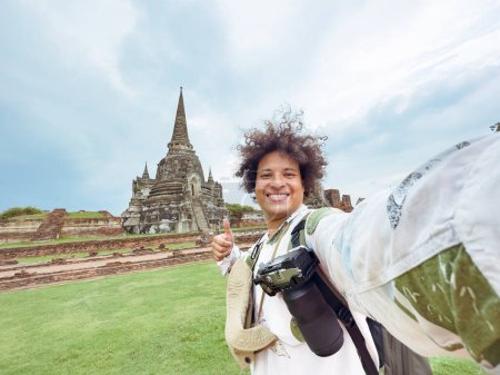 traveler with thumbs-up in front of towering Thai stupas, Enthusiastic Selfie at Ancient Thai temple