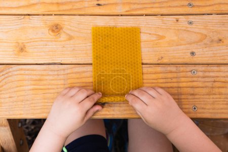 Top view of crop anonymous child rolling up beeswax and making candle at wooden table