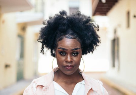Retrato de una bonita mujer negra con el pelo afro mirando a la cámara. Ella tiene algunos rasgos característicos y se ve confiada.