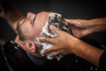 Téléchargez les photos : Salon de coiffure urbain moderne coiffeur lave les cheveux d'un client dans un salon de coiffure professionnel et studio. Vue détaillée en gros plan - en image libre de droit
