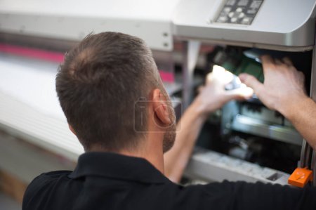 Téléchargez les photos : Toutes les machines sont entretenues. Technicien professionnel dépannage et réparation des machines dans l'imprimerie. - en image libre de droit