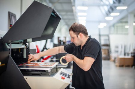 Photo for In the printing house, an experienced technician works on a UV printer. Production work. Check the print quality. - Royalty Free Image