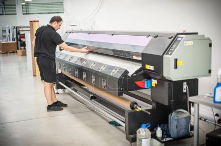 Téléchargez les photos : Dans l'imprimerie, un technicien expérimenté travaille sur une imprimante UV. Travail de production. Vérifiez la qualité d'impression. - en image libre de droit