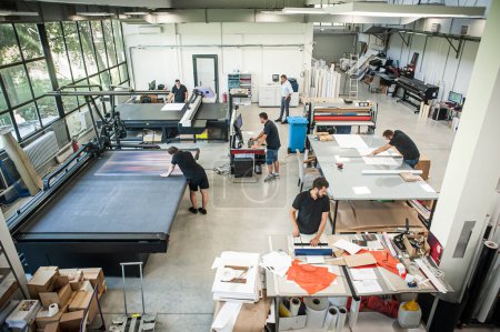 In a large modern printing plant, operators work on various types of machines for printed material