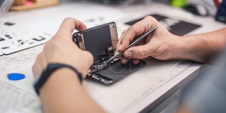 Photo for Workplace top view, close-up. In an electronics repair shop, a repairman repairs a smartphone, uses tweezers as one of the many work tools. - Royalty Free Image