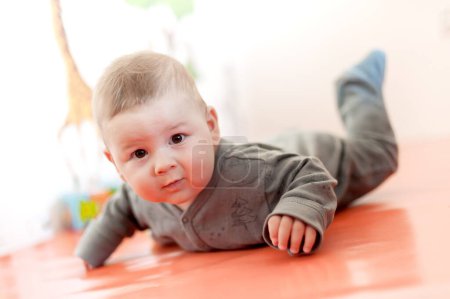 Téléchargez les photos : Cute baby boy lies on its stomach and crawls on the floor. Joy and happiness concept. Love and family emotion - en image libre de droit