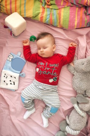 Téléchargez les photos : Un petit garçon mignon dort paisiblement et détendu sur son lit avec des jouets. Vue du dessus de la crèche. Amour et émotions familiales - en image libre de droit