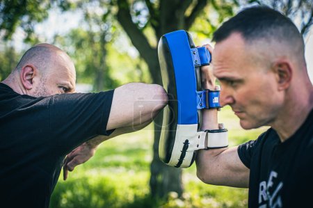 Foto de El entrenador Muay Thai tiene guantes de enfoque. Entrenamiento y demostración técnica de patada de codo con almohadillas. Práctica de artes marciales - Imagen libre de derechos