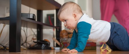 Téléchargez les photos : Bébé garçon mignon rampe sur le sol de la maison, explorer le monde et des choses autour de lui. Amour et émotion familiale - en image libre de droit