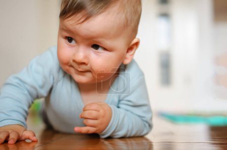 Téléchargez les photos : Bébé garçon mignon rampe sur le sol de la maison, explorer le monde et apprendre à bouger. Amour et émotion familiale - en image libre de droit
