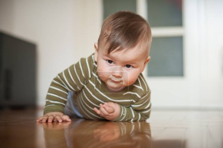 Téléchargez les photos : Bébé garçon mignon rampe sur le sol de la maison, explorer le monde et apprendre à bouger. Amour et émotion familiale - en image libre de droit