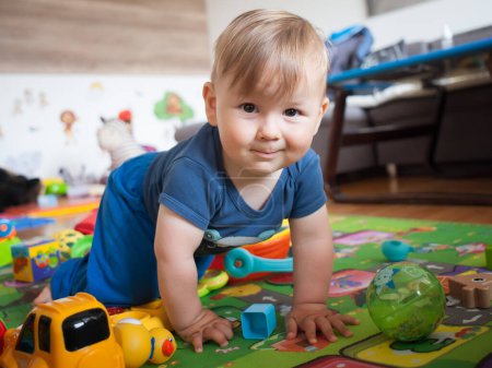 Téléchargez les photos : Bébé garçon mignon rampe et explorer les choses autour, entouré de jouets colorés. Amour et émotion familiale - en image libre de droit