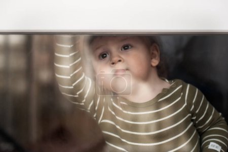 Téléchargez les photos : Portrait de mignon petit garçon avec jouet en peluche regardant par la fenêtre, regardant triste. Amour et émotion familiale - en image libre de droit