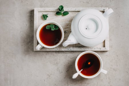 Deux tasses de thé à la menthe et une théière sur un plateau de marbre gris.