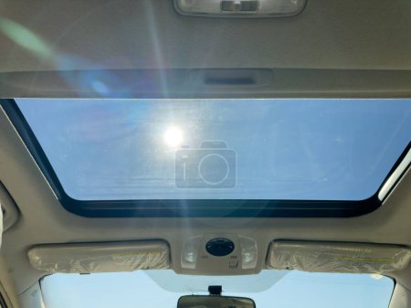 View of the clear sky through the open sunroof hatch of a car on a sunny day.