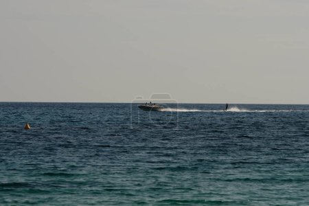 Foto de Ios, Grecia: 30 de mayo de 2021: Turistas siendo arrastrados a través del mar por un barco en una moto de agua en la famosa playa de Mylopotas en Ios Grecia - Imagen libre de derechos